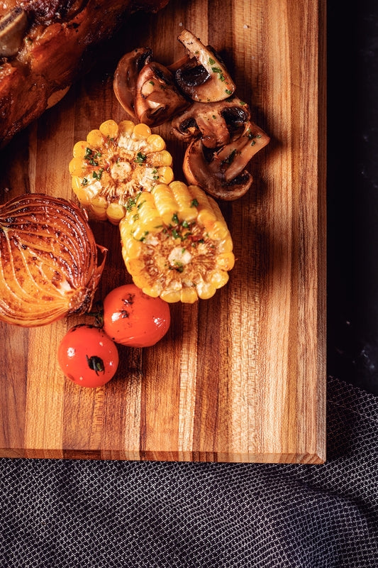 Tabla de madera con verduras asadas: mazorcas de maíz, champiñones, cebolla y tomates cherry