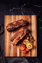 Costillas asadas con maíz, tomates cherry y champiñones sobre tabla de madera