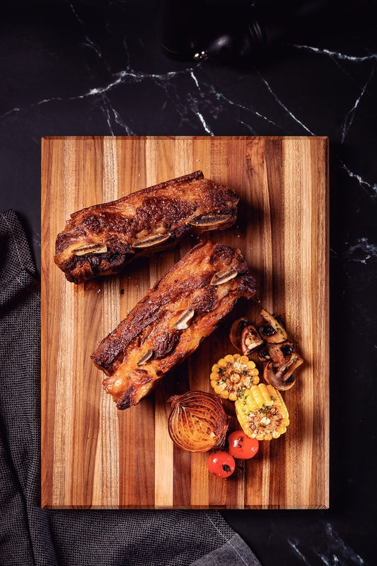 Costillas asadas con maíz, tomates cherry y champiñones sobre tabla de madera