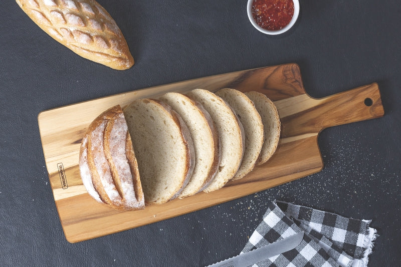 Tabla de madera con pan rebanado, pan entero, bowl de mermelada y cuchillo
