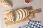 Tabla de madera Tramontina con pan rebanado, baguette, cuchillo y paño a cuadros sobre superficie beige