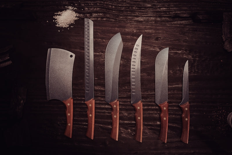 Set de seis cuchillos de cocina con mangos de madera y hojas de acero inoxidable sobre superficie de madera oscura