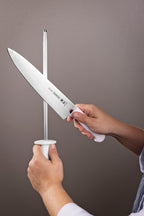 Cuchillo de acero inoxidable con mango blanco sostenido junto a un chaira, marca Tramontina visible en el filo