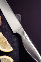 Cuchillo de acero inoxidable con mango metálico sobre superficie de pizarra oscura, acompañado de rodajas de limón