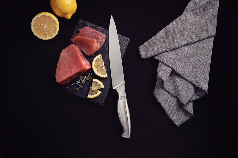 Cuchillo de acero inoxidable sobre tabla oscura con trozos de pescado crudo, rodajas