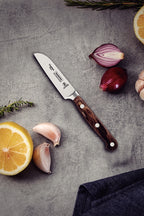 Cuchillo Tramontina con mango de madera sobre superficie gris, acompañado de limón, ajo, cebolla morada y rom