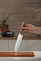 Cuchillo santoku Tramontina con mango negro y hoja de acero inoxidable con alveolos, sostenido sobre tabla de madera
