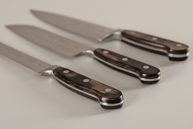 Juego de tres cuchillos de cocina con mangos de madera oscura y remaches metálicos sobre superficie clara