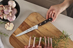 Cuchillo Tramontina Century con mango de madera sobre tabla de cortar, junto a ajos, romero y rack de cordero